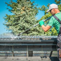 Roof and Gutters Power Cleaning Using Pressure Washer. Caucasian Worker.
